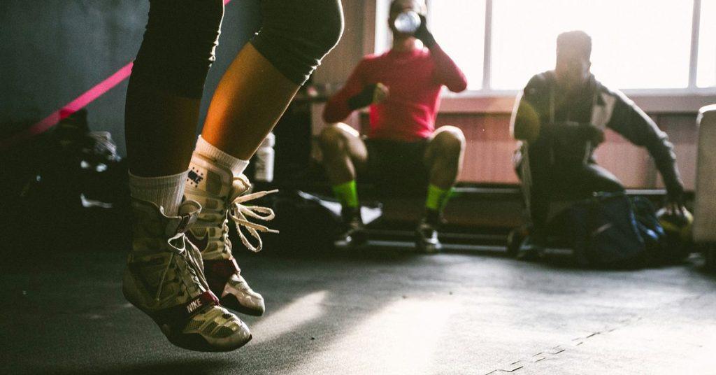 Athlete jumping rope in a gym while others rest and rehydrate, illustrating exercise recovery
