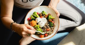 Woman eating a colorful quinoa, broccoli, and tomato bowl, illustrating foundational nutrition