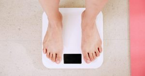 Bare feet standing on a white bathroom scale, illustrating the FTO gene and weight